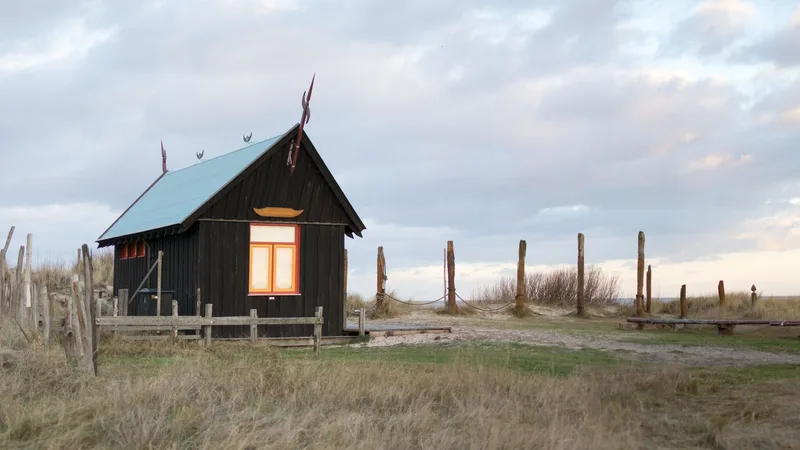 Een donker houten huisje in de duinen met een verlicht raam
