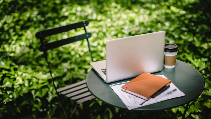 Laptop, notitieboek en koffie op een tuintafel tussen het groen